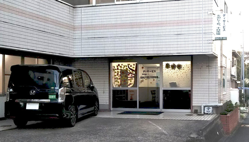 介護施設の玄関・車寄せ。駐車スペース付き、タイル張り外壁で清潔感がある。