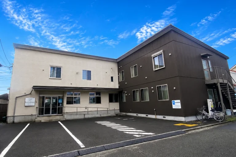 株式会社ウェルフューチャーの、スロープ付き玄関と駐車場に車椅子が置かれた、明るい介護施設の外観。