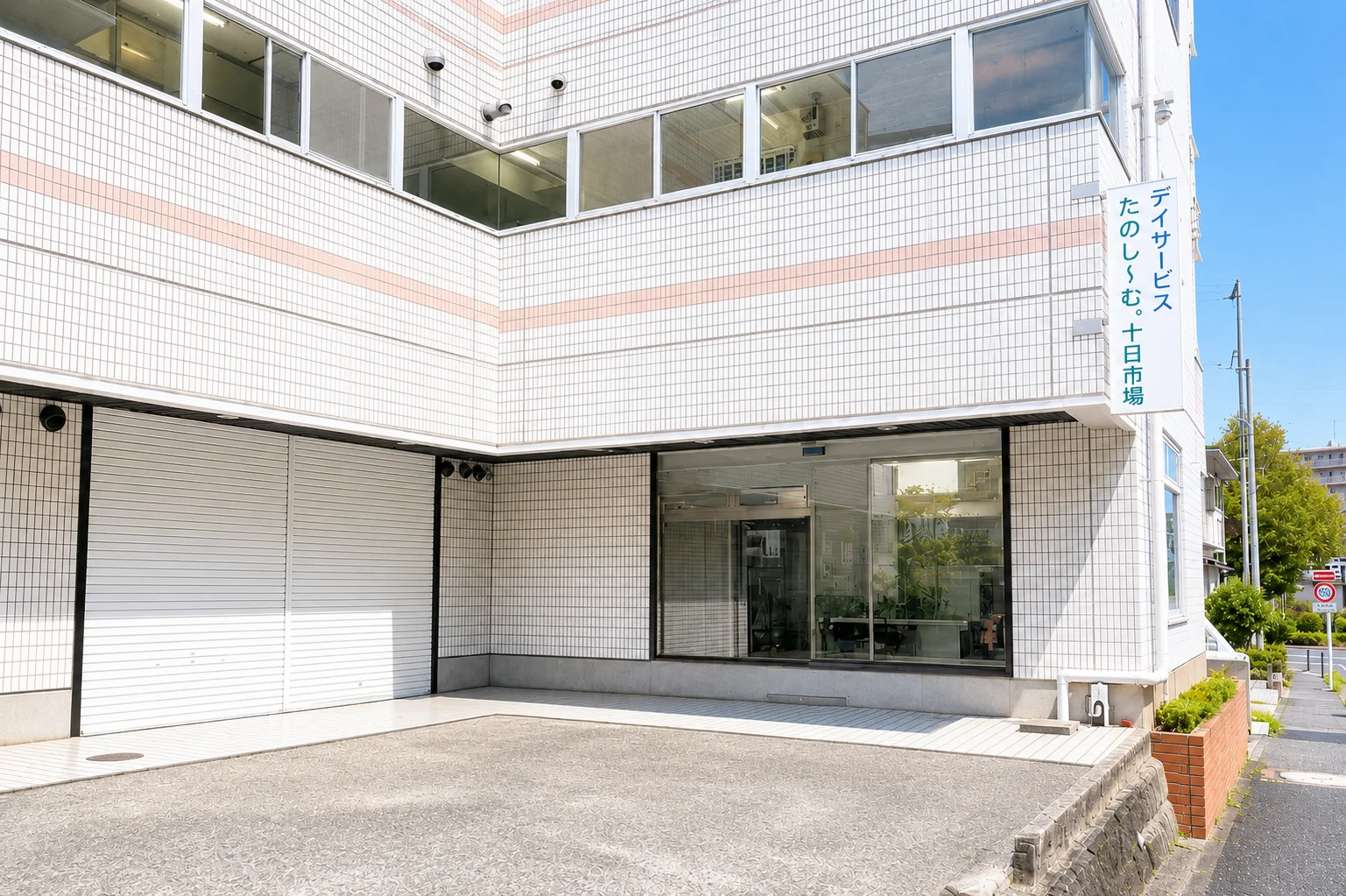 株式会社ウェルフューチャーが運営するデイサービスたのし〜む。十日市場の看板を掲げた、白いタイル壁とエントランスが特徴の介護施設外観。