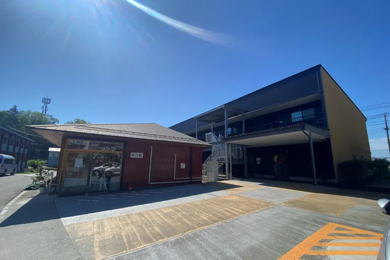 青空の下、受付棟とモダンな多層の建物が並ぶ、株式会社ウェルフューチャーの介護福祉施設の外観。